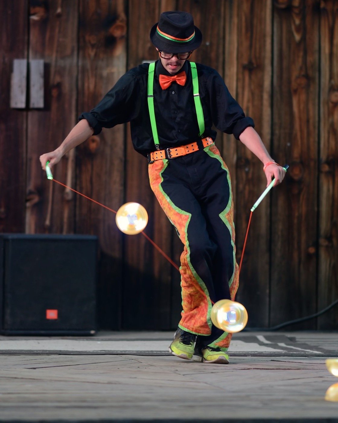 Circus performer in a hat and bright suspenders spinning two diabolos on stage
